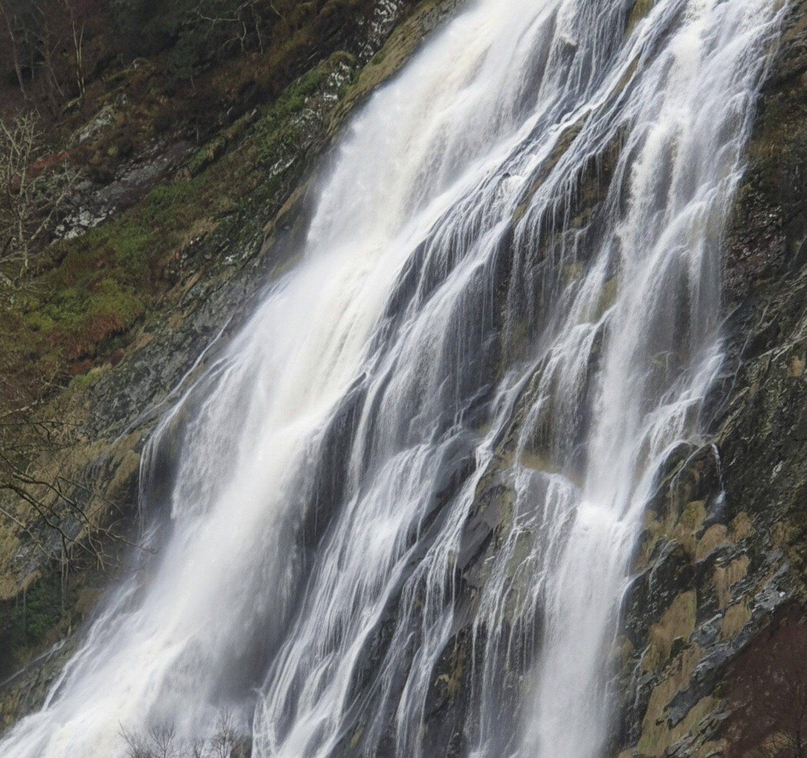 A wide waterfall in spate, breaking white over dark, tiered rock