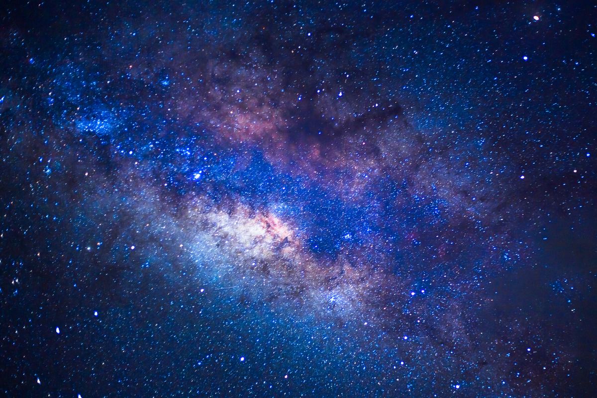 A close night-sky photograph of the Milky Way's core: dense blue and violet star fields crossed by pale luminous dust and darker lanes, filling the whole frame with no horizon in view.