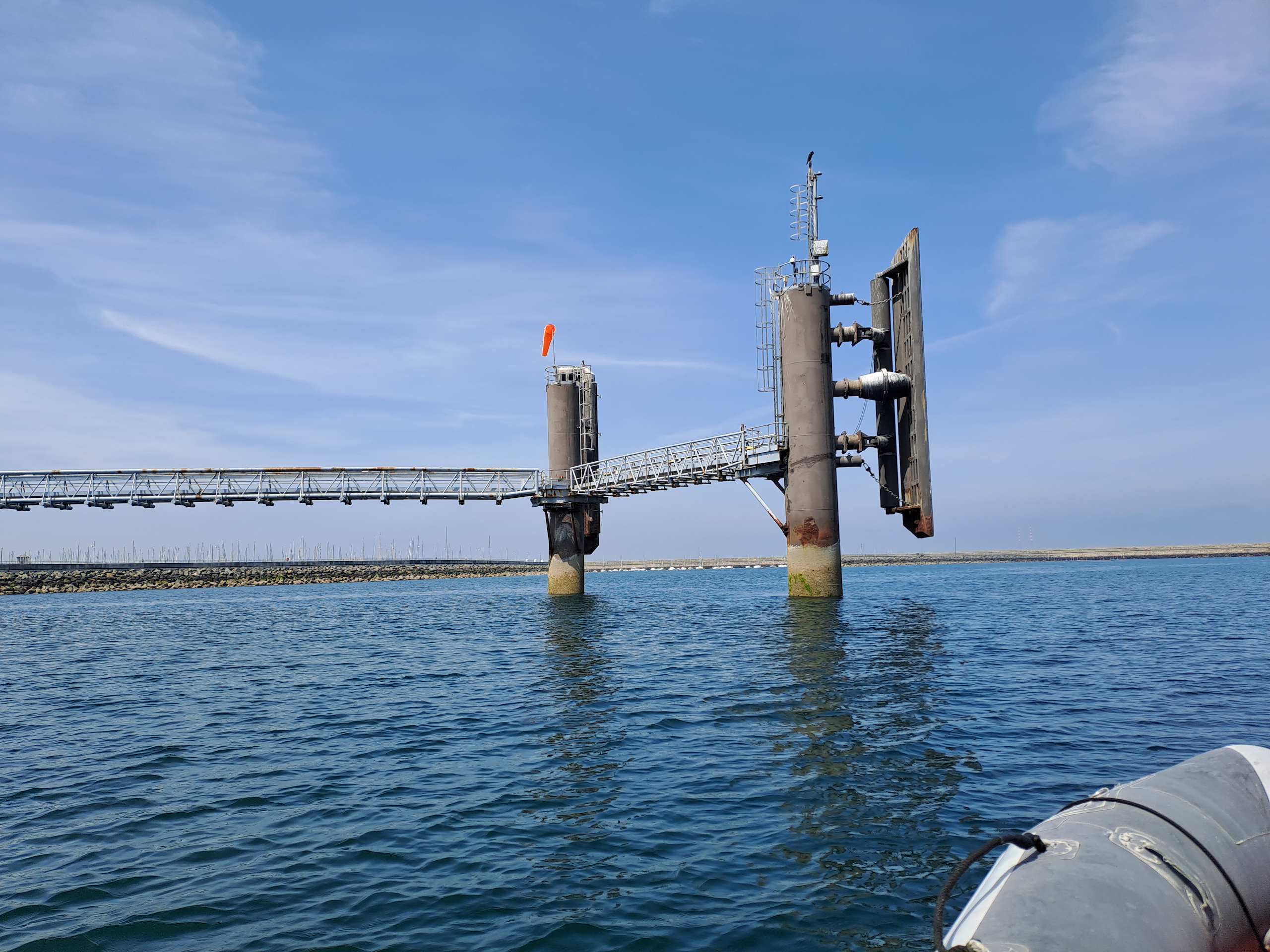 A mooring gantry tower rising from Saltmere's open water, its truss causeway running out toward a floating city segment beyond the frame